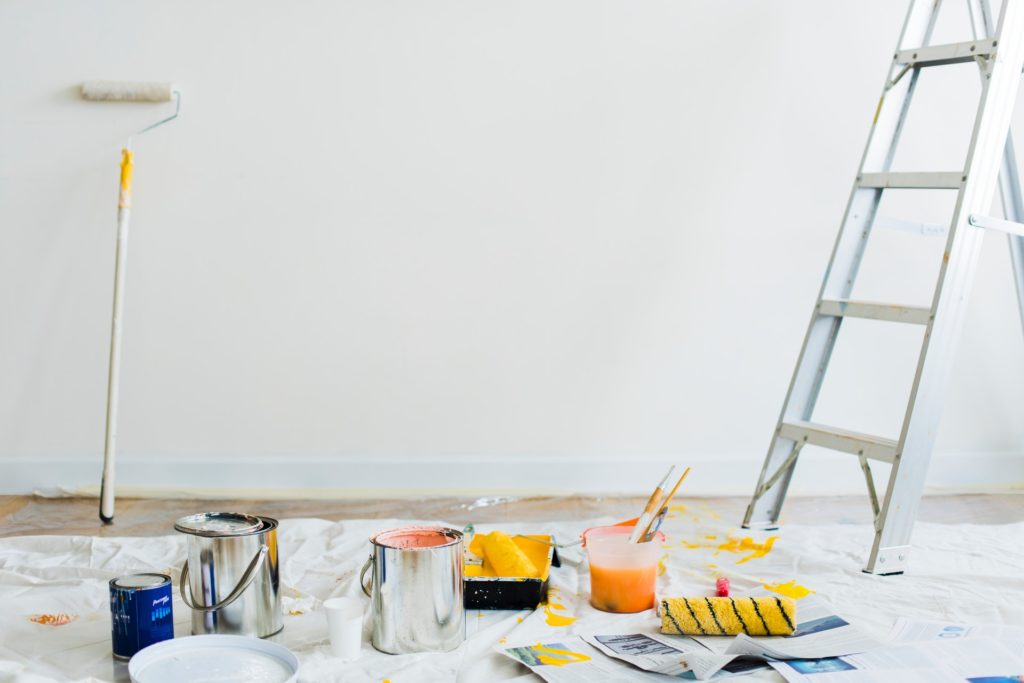 Paint roller, paint cans, and ladder against a white wall