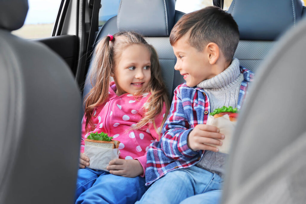 Alt text: Two kids smiling eating sandwiches in a car.