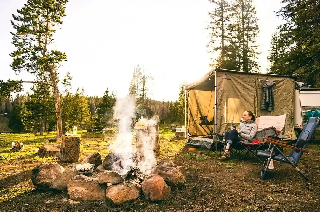Person relaxing by a campfire beside a tent in a forested campsite in British Columbia, Canada