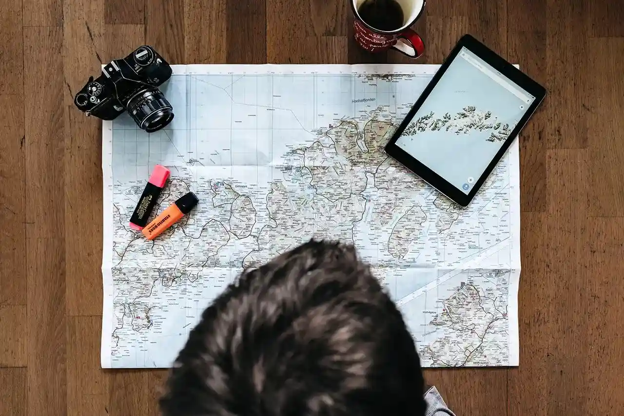 Person reviewing a travel map with a camera and tablet on a wooden table in British Columbia, Canada